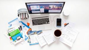 Een rommelig bureau met brochures van internetproviders en een laptop.